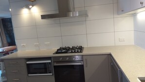 A modern kitchen with a gas stove, built-in oven, microwave, and stainless steel cabinets. - The Pink Pipi Karitane (Karitane)