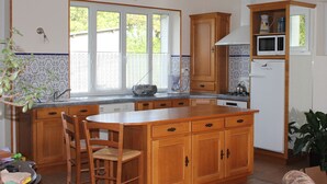 Une cuisine avec des meubles en bois, un îlot central, une table à manger avec des chaises et une fenêtre donnant sur un espace verdoyant.