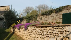 Un mur de pierre avec un parterre fleuri où poussent des fleurs violettes et une porte verte.