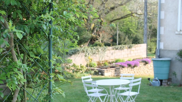 Un jardin avec une table et des chaises en métal blanc, entouré d’herbe verte et de plantes.