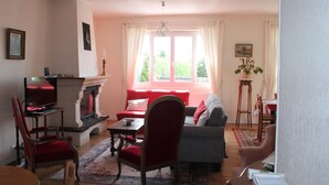 Un salon avec une cheminée, des canapés rouges et gris, un fauteuil rouge, une table basse en bois et un tapis à motifs.