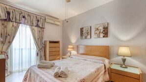 A neatly arranged bedroom with a bed, bedside lamps, a dresser, and a window with curtains.