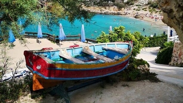 A boat parked by a beach with clear blue water and rocky cliffs in the background.