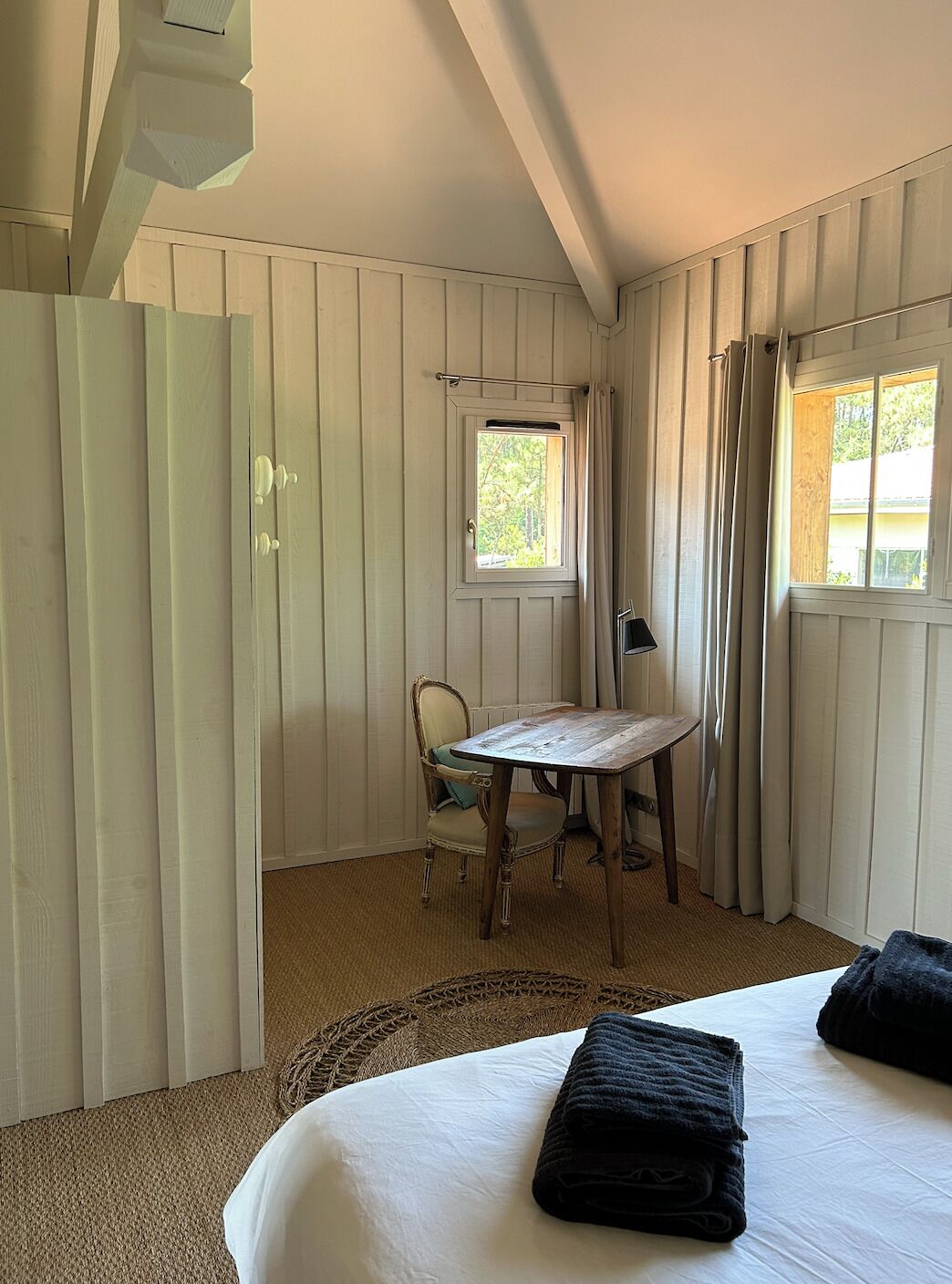 A bedroom with a bed, a chair, a small table, and a window.