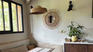 Et hyggeligt rum med en træbænk, et lille bord, et rundt spejl og en potteplante.
