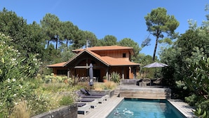 Et træhus med swimmingpool, omgivet af grønt og træer.