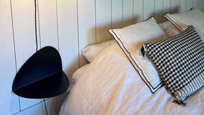 Et soveværelse med en seng, en hængende lampe og to billeder i rammer på væggen.