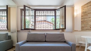 Un sofá gris con dos cojines, una mesa blanca y una ventana con una reja de metal.