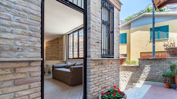 Un espacio habitable diáfano con sofá, mesa de comedor y zona de cocina visible a través de un arco.