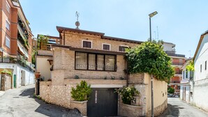 Una calle estrecha con un edificio que presenta una reja negra, muros de piedra y plantas en macetas.
