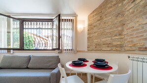 Una sala de estar moderna con un sofá gris, sillas blancas, una mesa redonda con individuales rojos y una pared de ladrillo.