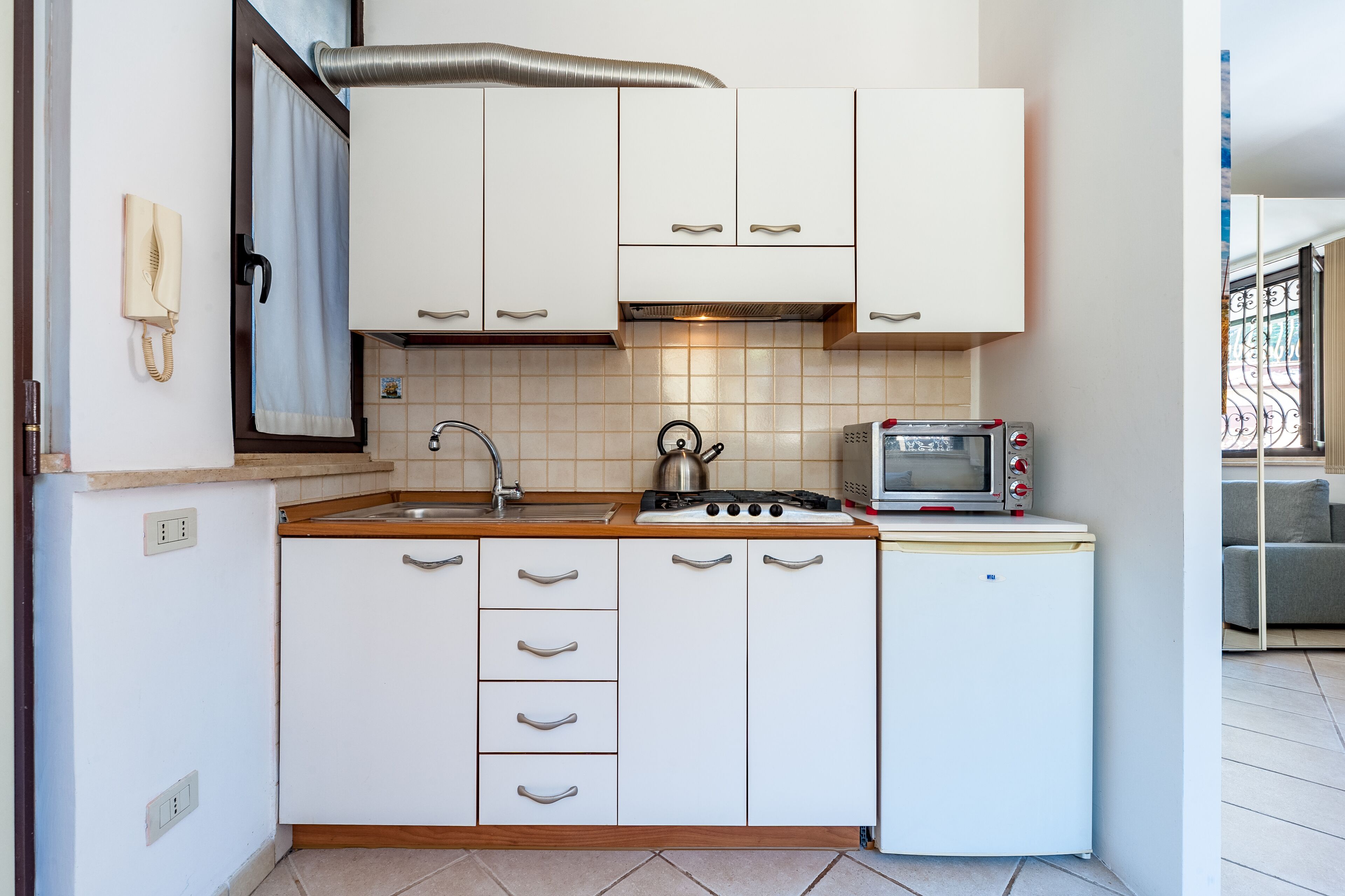 Eine kleine Küche mit weißen Schränken, einer Spüle, einem Herd und einem kleinen Kühlschrank.