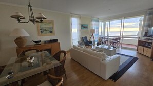 Ein geräumiger Wohnbereich mit einem Glastisch, einem weißen Sofa und einem Balkon mit Meerblick.