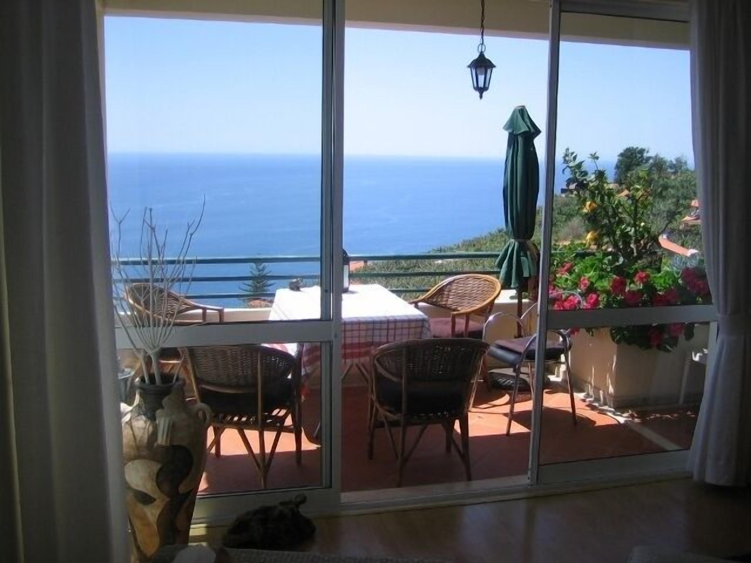 A balcony with wicker chairs, a table, and a view of the sea.