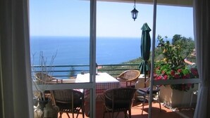 Ein Balkon mit Korbstühlen, einem Tisch und Blick auf das Meer.