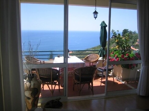 A balcony with wicker chairs, a table, and a view of the sea.