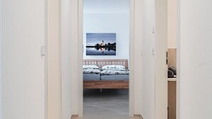 A narrow hallway leading to a bedroom with a bed, a nightstand, and a wall-mounted TV. - Exclusive new apartments with a romantic location at the small sailing port ( Überlingen)