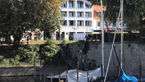 A waterfront property with a white building, a dock with boats, and a stone wall. - Exclusive new apartments with a romantic location at the small sailing port (Überlingen)