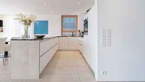 A modern kitchen with white cabinetry, a central island, and a window with blinds. - Exclusive new apartments with a romantic location at the small sailing port (Überlingen)