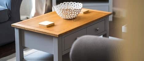A small wooden table with a white perforated bowl and a book on it, a gray chair, and a gray cabinet in the background.