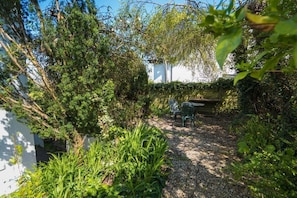 Un giardino con un vialetto ghiaioso, una recinzione in legno e un tavolo in metallo con sedie.