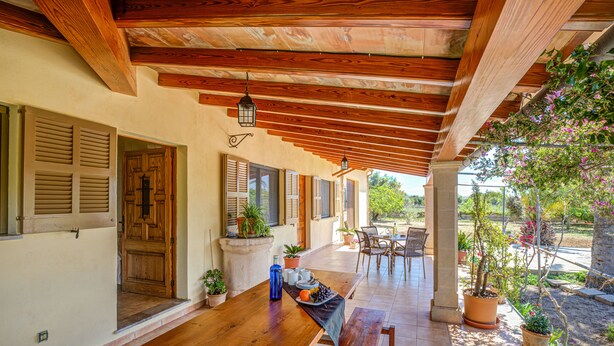 A wooden deck with a bench, potted plants, and a table with a tray of fruit and a bottle. - Villa Can Lluc(Private villa with big barbecue) (Puerto de Pollença)