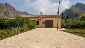 A stone pathway leading to a building with a tiled roof, surrounded by greenery and mountains in the background. - Villa Can Lluc(Private villa with big barbecue) (Puerto de Pollença)