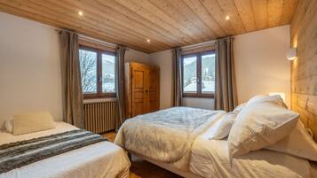 Een slaapkamer met twee bedden, een houten plafond, grote ramen en een houten garderobe.