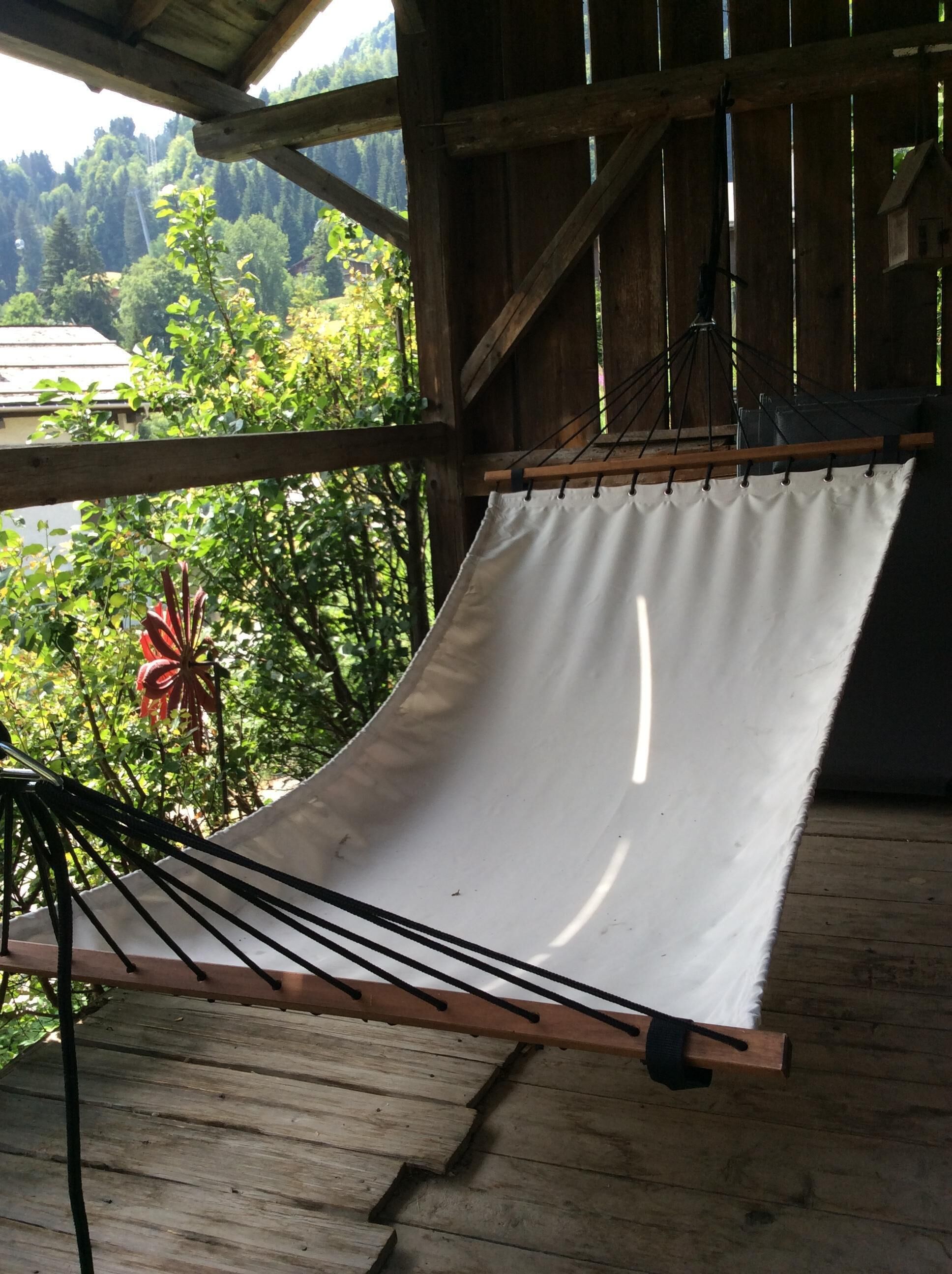 A hammock under a wooden structure with a view of a forested area.
