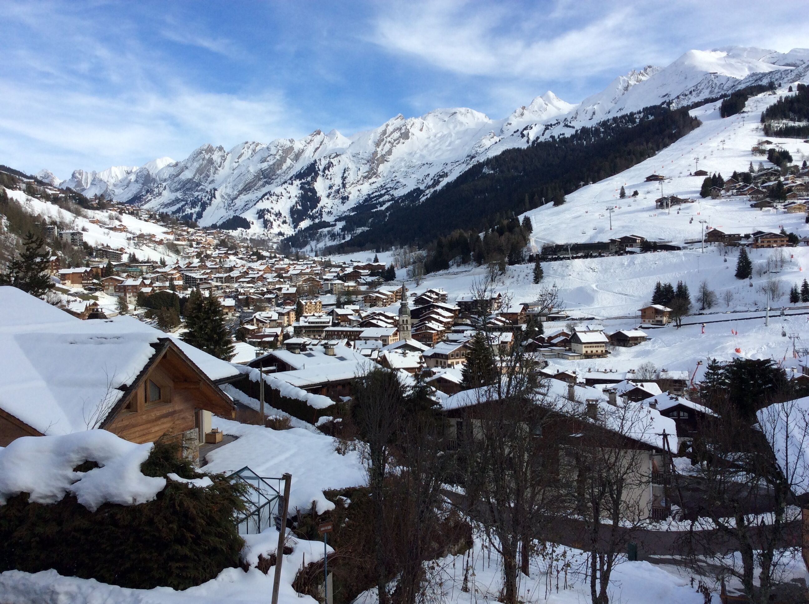 Ein verschneites Bergdorf mit traditionellen Holzhäusern, einer Skipiste und freiem Blick auf die umliegenden Gipfel.