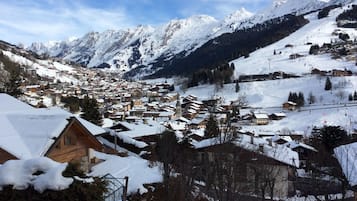 Ein verschneites Bergdorf mit traditionellen Holzhäusern, einer Skipiste und freiem Blick auf die umliegenden Gipfel.