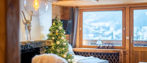 Een gezellige kamer met een open haard, een kerstboom en een groot raam met uitzicht op een besneeuwd landschap.