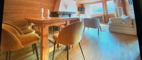 Ein Zimmer mit Holzboden, einem Esstisch mit Stühlen, einer Couch und einem großen Fenster.