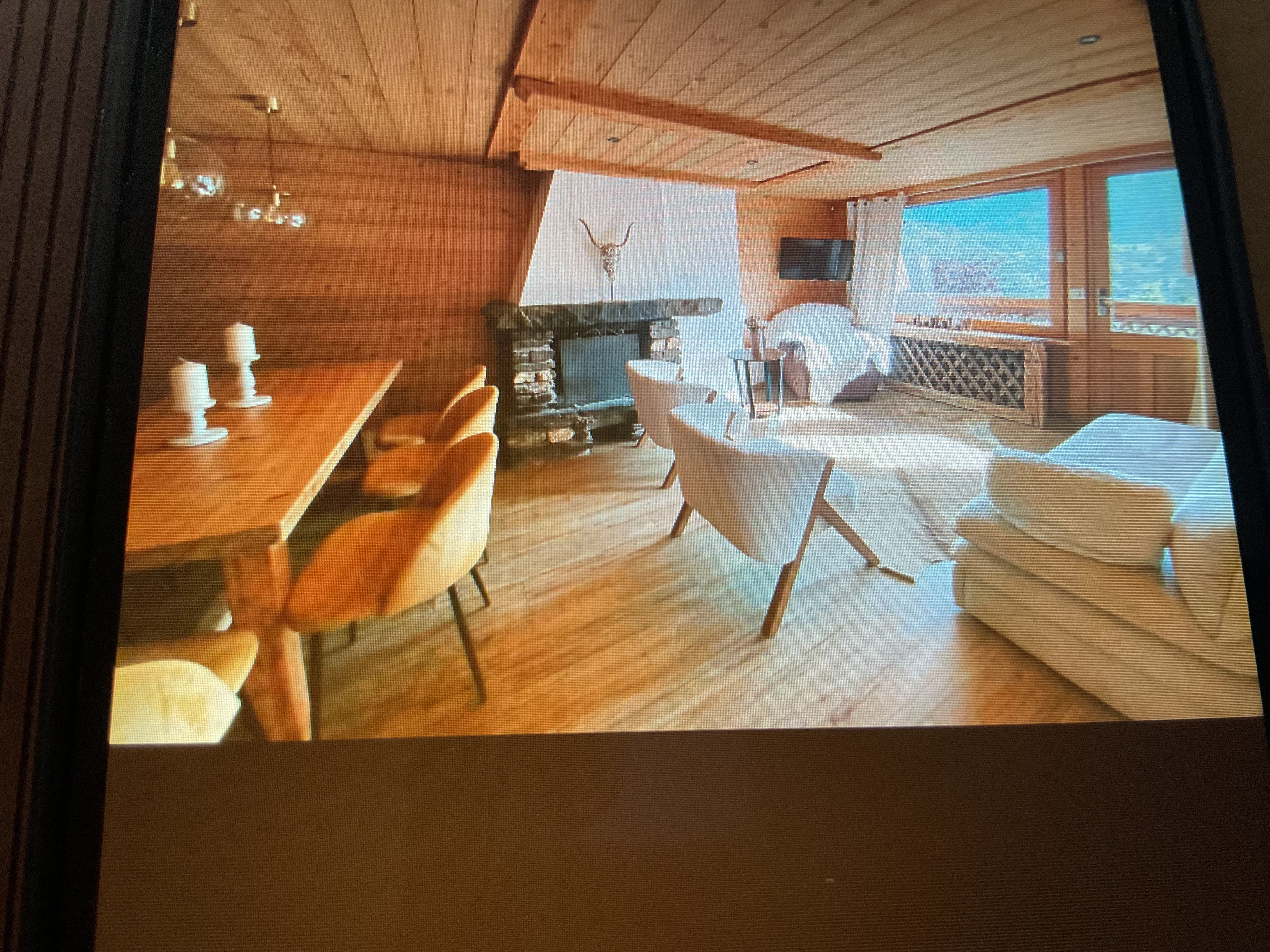 A room with a wooden ceiling, a fireplace, a dining area with chairs, and a view through a window.