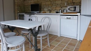 Eine kleine Küche mit Steinwand, einem weißen Tisch mit Stühlen und Standardgeräten wie Mikrowelle, Geschirrspüler und Backofen.