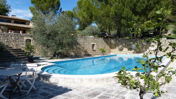 A swimming pool with stone steps leading up to a stone wall, surrounded by greenery and a building with a tiled roof. - Large self-contained studio with swimming pool in a nest of greenery in the heart of the Luberon (Saignon)
