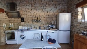 Eine kleine Küche mit Steinwand, einer Waschmaschine, einer Mikrowelle, einem Kühlschrank und einem Tisch mit einer Flasche und einer Tasche.