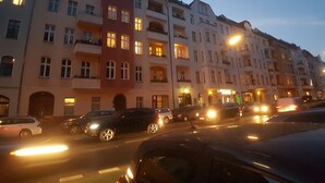 Straßenansicht mit mehrstöckigen Gebäuden, parkenden Autos und Straßenlaternen.