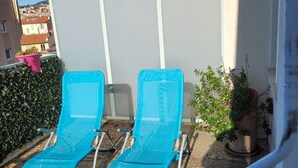 Deux fauteuils bleus sont placés sur une terrasse carrelée, agrémentée de plantes en pot, avec un mur blanc en arrière-plan.