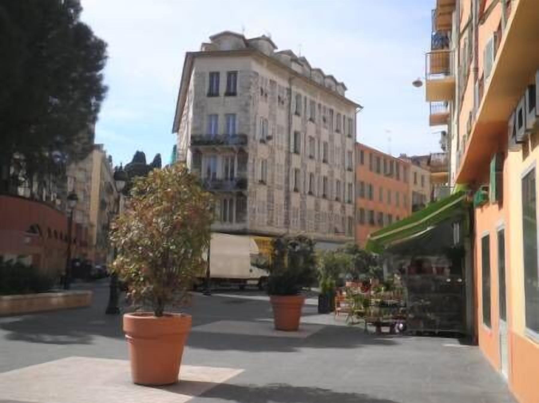 A street with buildings, potted plants, and a clear sky.