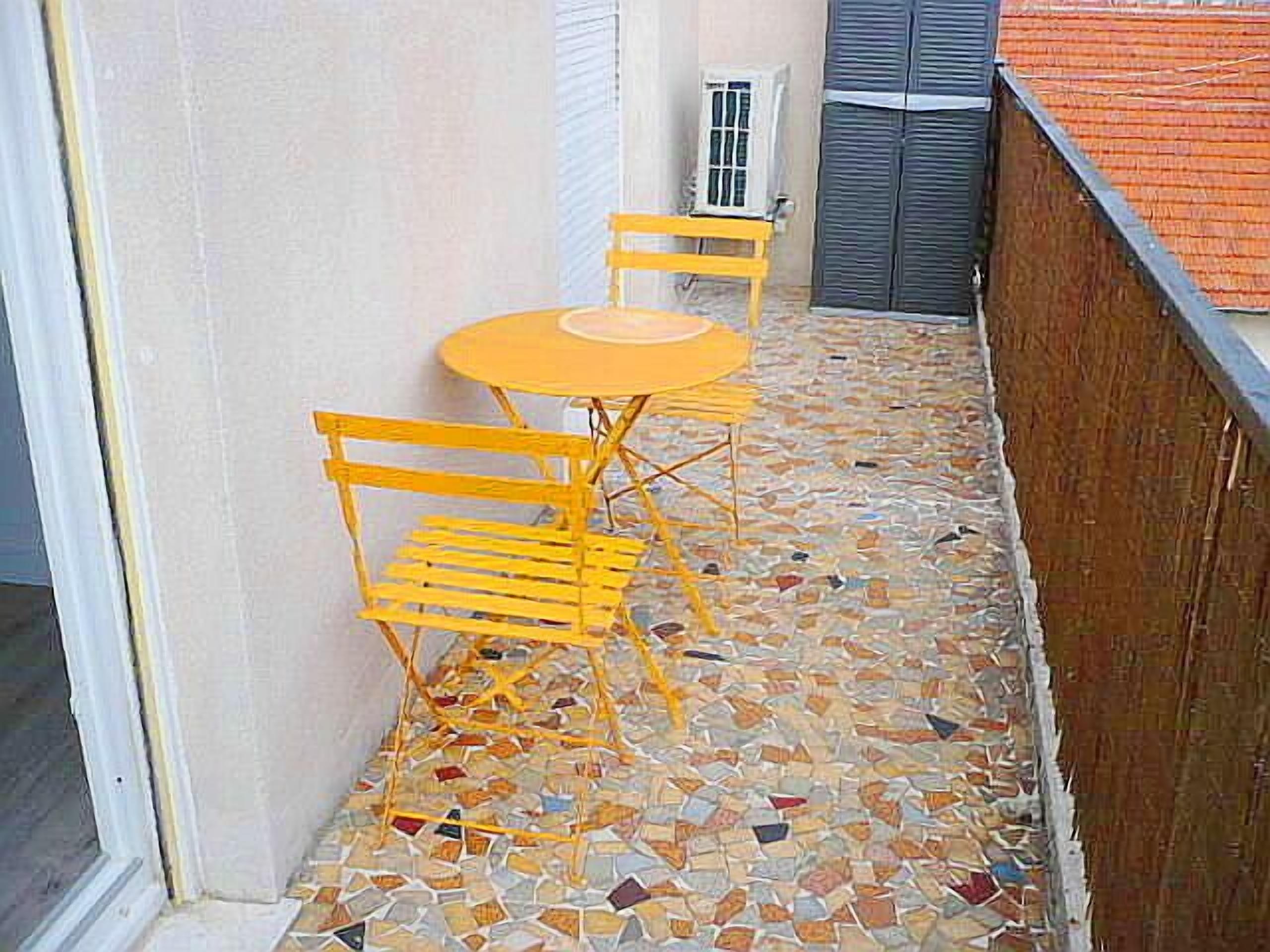 A small outdoor patio with a mosaic floor, a yellow table, and two yellow chairs.