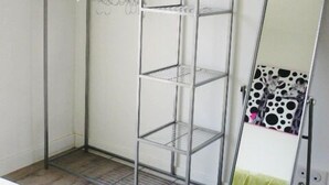 Une armoire en métal avec plusieurs étagères et une tringle pour suspendre les vêtements, un grand miroir et un coussin à motifs posé sur le sol.