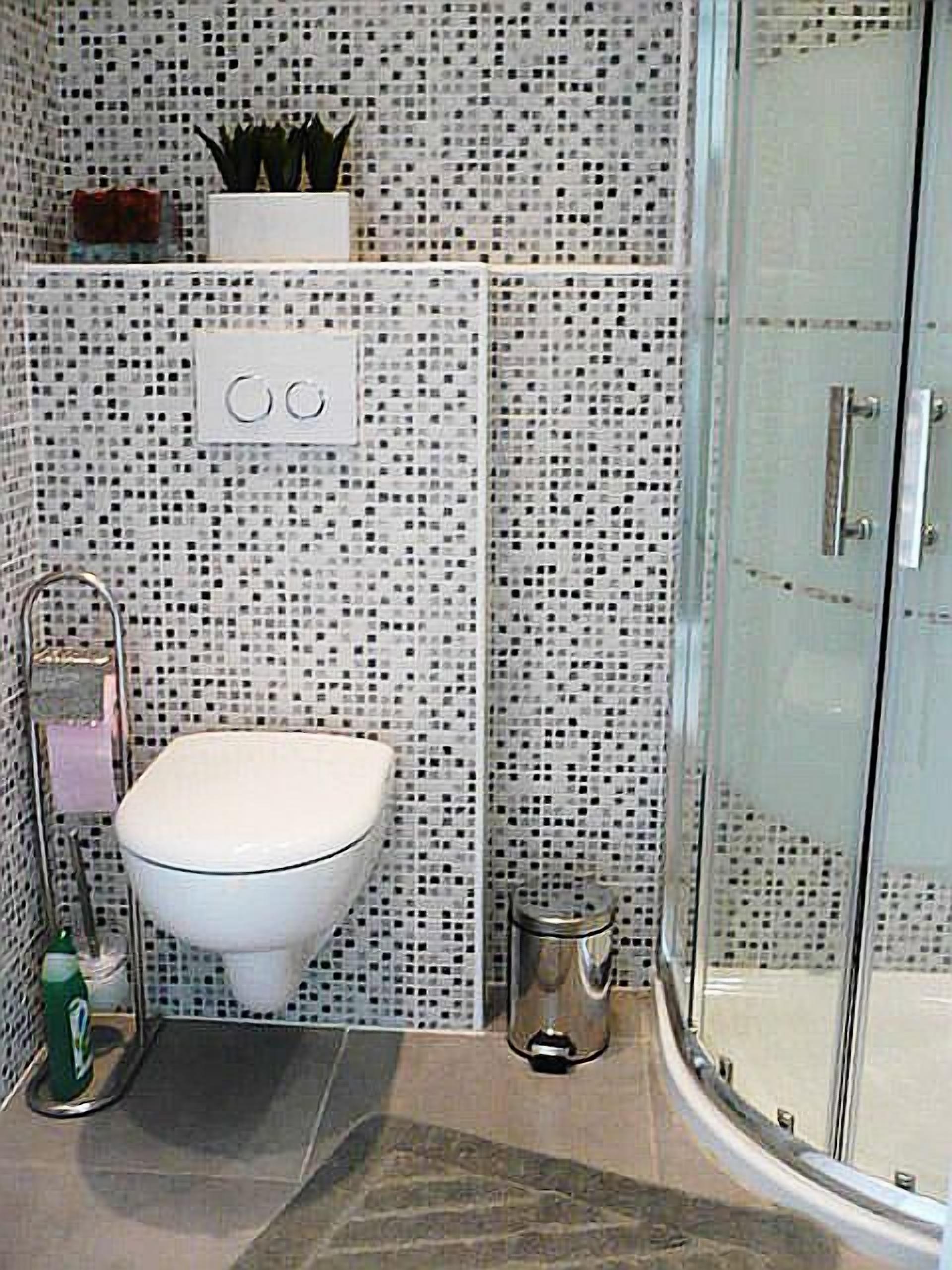 A bathroom with a toilet, a small trash bin, and a shower area.