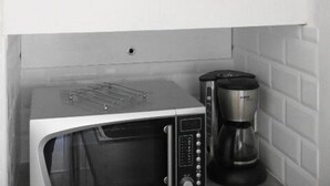 Une cuisine équipée d’un four à micro-ondes, d’une machine à café et ornée d’un tableau représentant une scène de plage.