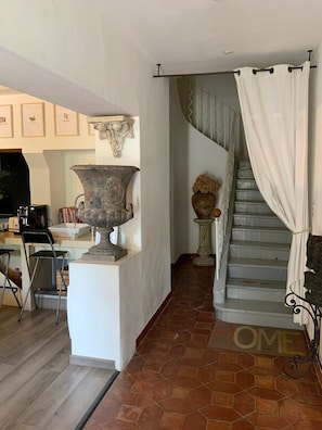 Un escalier orné d’une enseigne indiquant « MAISON », un grand vase et une sculpture fixée au mur.