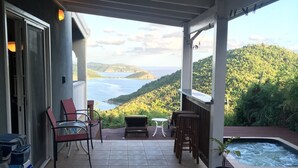 A covered outdoor area with a view of the sea, a hot tub, and outdoor furniture.