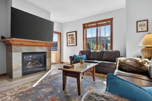 A living room with a fireplace, a sofa, a coffee table, and a large window. - Special Luxury Resort Pool Hot Tubs Walk to it all (Breckenridge)