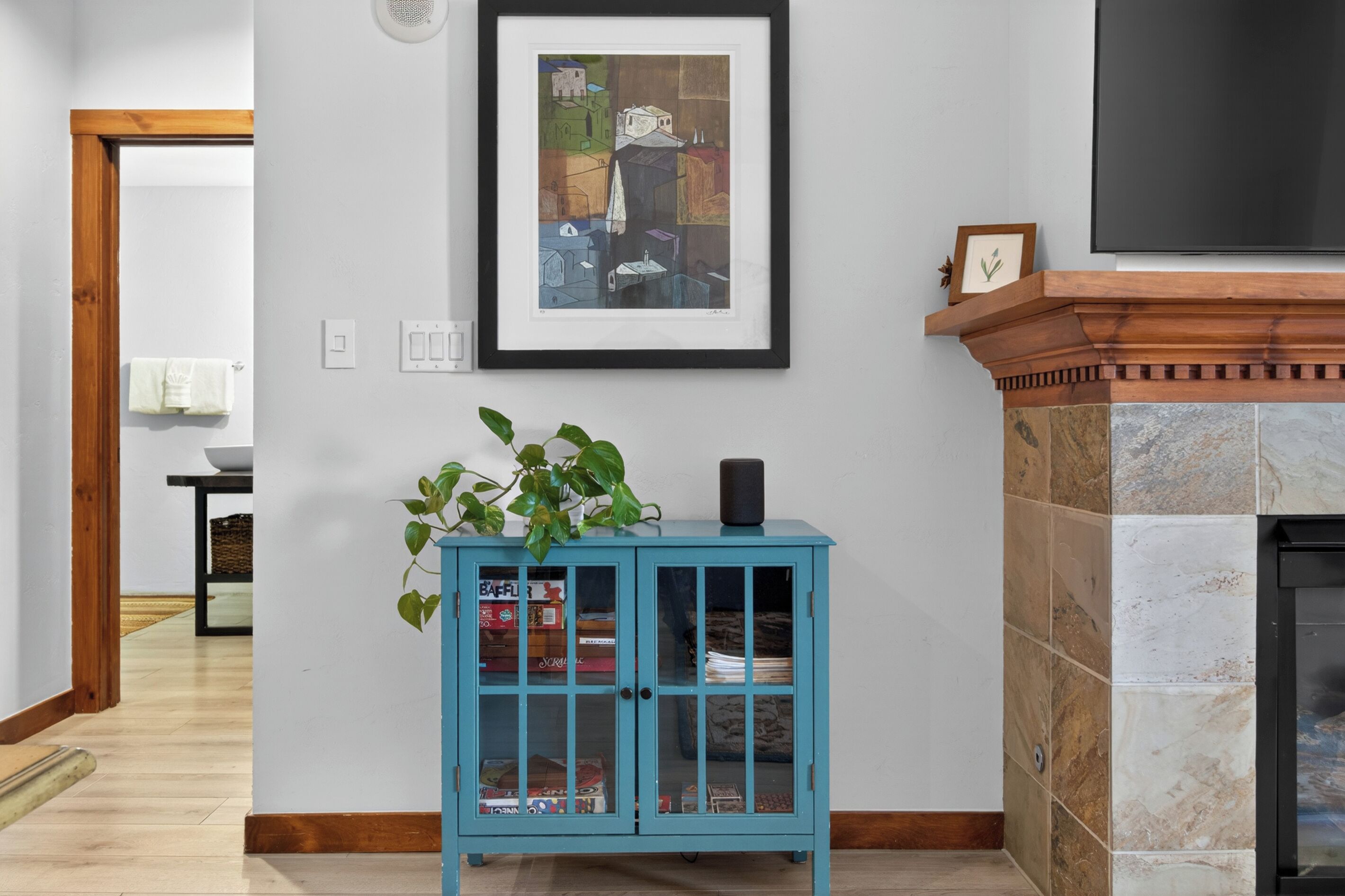 Une pièce avec un meuble bleu, une cheminée et une œuvre d’art encadrée au mur.