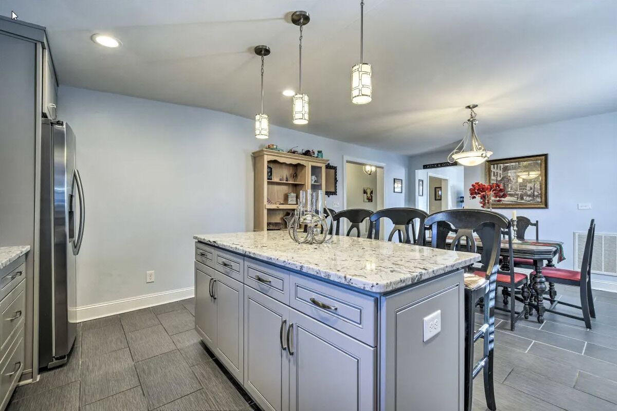 A kitchen with a central island, a dining area with chairs, and a refrigerator.