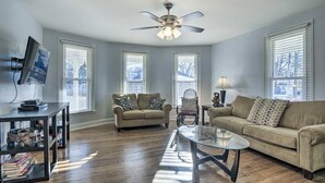A spacious living room with a ceiling fan, two sofas, a coffee table, and a TV on a stand. - Cottage on the Boulevard - Renovated, Historic Downtown Wendell-3 Beds, 2 Baths (Wendell)